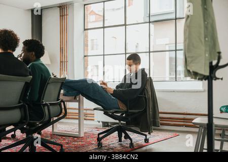 Non-binary business professional sitting with feet up on chair while working in tech hub Stock Photo