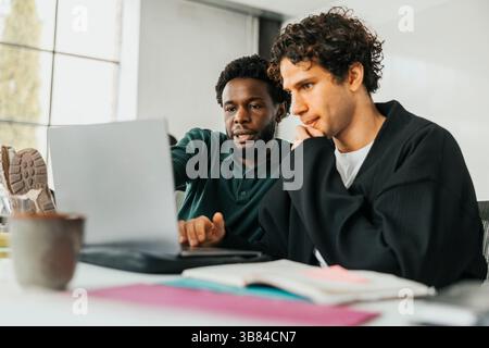 Male IT professionals discussing over laptop while sitting at desk in office Stock Photo