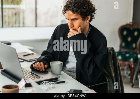 Thoughtful male software engineer working on laptop while sitting at desk in work place Stock Photo