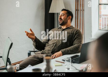 Happy businessman gesturing while sitting on chair at desk in work place Stock Photo