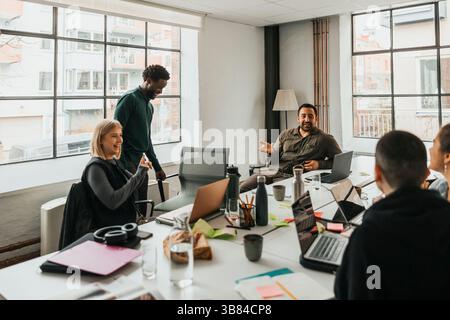 Smiling male and female business professionals talking with each other while sitting in meeting room at work place Stock Photo