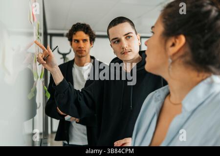 Non-binary business professional pointing on whiteboard while talking with colleague during discussion in office Stock Photo