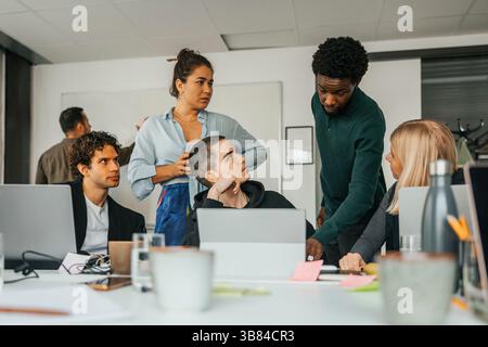 Young businessman sharing ideas while explaining through laptop to coworkers at work place Stock Photo