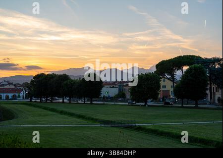 Sunset over the city of Lucca, Tuscany, viewed from the historic walls. The sun sets behind the Tuscan hills, casting a golden glow over rooftops and Stock Photo