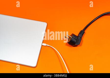 A Gray tablet connected with a white cable and a black cable on an orange surface.  Stock Photo