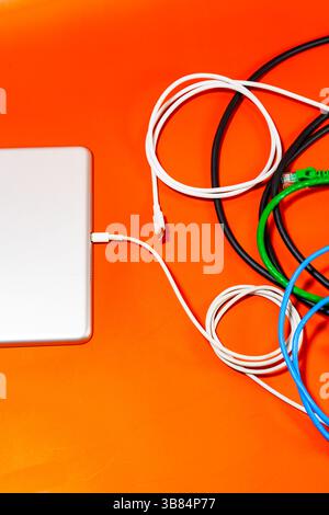 Flat lay composition of modern ultra slim gadget connected with USB cable among various colored wires placed on orange background in light Stock Photo