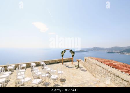 White chairs stand in front of a wedding arch on an observation deck overlooking the sea. Stock Photo