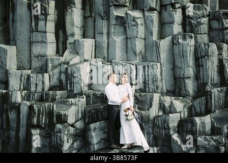 Bride and groom stand on the black rocks of Reynisdrangar in Iceland. Stock Photo