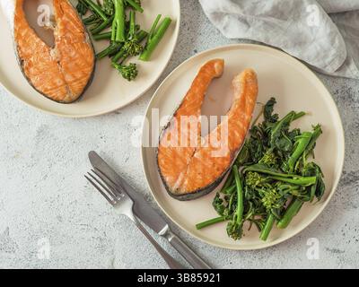 Ready-to-eat grilled salmon steak and greens - baby broccoli or broccolini and spinach on rustic craft plate over gray background. Keto diet dish. Top Stock Photo