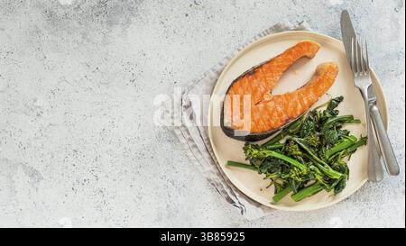 Ready-to-eat grilled salmon steak and greens - baby broccoli or broccolini and spinach on rustic craft plate over gray background. Keto diet dish. Top Stock Photo
