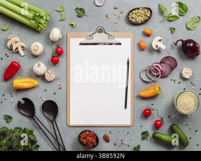 Food ingredients, salad serving utensils and clipboard with white paper sheet. Various of vegetarian cooking ingredients on gray background.Recipe boo Stock Photo