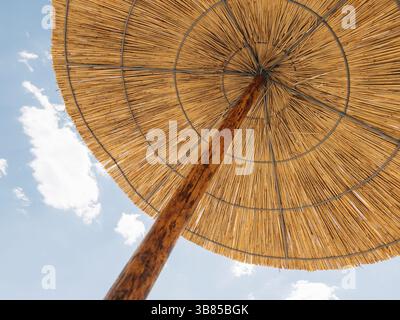 Straw sun umbrella against cloudy sky. Stock Photo