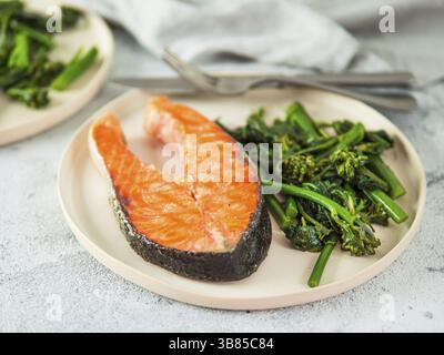 Ready-to-eat grilled salmon steak and greens - baby broccoli or broccolini and spinach on rustic craft plate over gray background. Keto diet dish Stock Photo