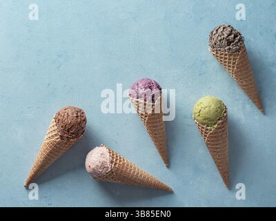 Various ice cream scoops in cones with copy space. Colorful ice cream in cones chocolate, strawberry, blueberry, pistachio or matcha, biscuits chocola Stock Photo