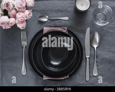 Beautiful table setting on gray linen tablecloth. Festive table setting for wedding dinner with pink spray roses and scented cabdle. Holiday dinner wi Stock Photo