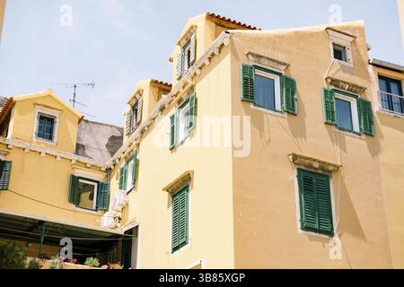 Large beige residential building with windows and green shutters on a sunny day. Stock Photo