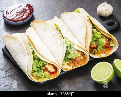 Three homemade tacos with chicken, vegetables and salsa. Latin food tacos on black wooden cutting board over black table Stock Photo