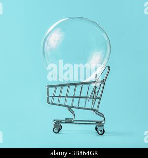 Shopping cart with soap bubble on bright blue background. Ephemeral happiness from shopping, shopaholism, consumerism concept. Shopping concept, minim Stock Photo