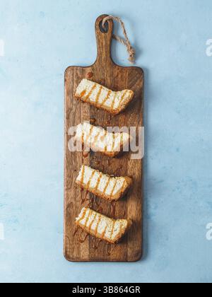 Caramelized cheesecake slices on wooden cuttingboard. Cheesecake on blue background with copy space for text. Top view or flat lay. Vertical Stock Photo
