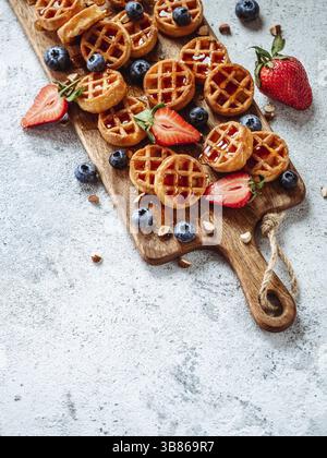 Small round delicious soft belgian waffles on cutting board. Fresh belgian waffles with berries and caramel sauce top view. Copy space for text or moc Stock Photo