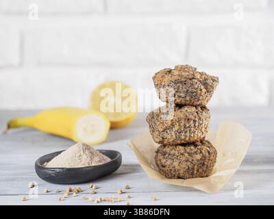Healthy gluten-free homemmade banana muffins with buckwheat flour. Stack of three vegan muffins with poppy seeds and lemon on gray wooden table. Copy Stock Photo