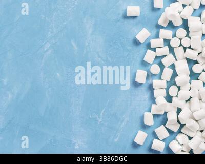 Marshmallows on blue background with copyspace. Flat lay or top view. Background or texture of colorful mini marshmallows. Winter food background conc Stock Photo