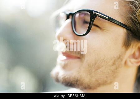 Young man with glasses squints at the sun. Profile. Portrait. Stock Photo