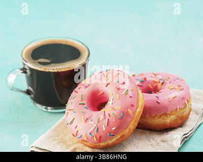 Two pink donuts and coffee on blue concrete background with copy space. Colorful donuts and coffee cup with copyspace. Glazed doughnuts with sprinkles Stock Photo