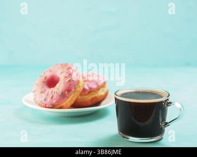 Two pink donuts and coffee on blue concrete background with copy space. Colorful donuts in plate and coffee cup with copyspace. Glazed doughnuts with Stock Photo