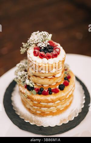 Wedding white bunk cake decorated with berries and flowers on the table. Stock Photo