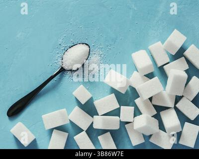 Background of sugar cubes and sugar in spoon. White sugar on blue background. Sugar with copy space. Top view or flat lay Stock Photo