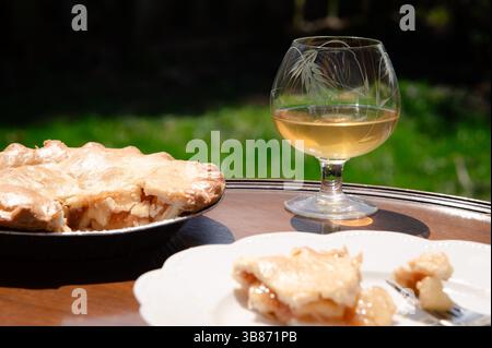 Apple pie and a glass of wine on a wood table outside on a sunny day Stock Photo