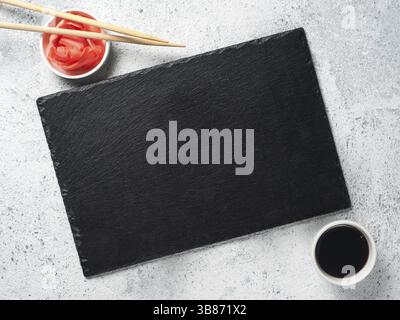 Empty slate plate on gray cement background with chopsticks, pickled ginger and soy sauce. Copy space. Top view or flat-lay. Concept for restaurant an Stock Photo