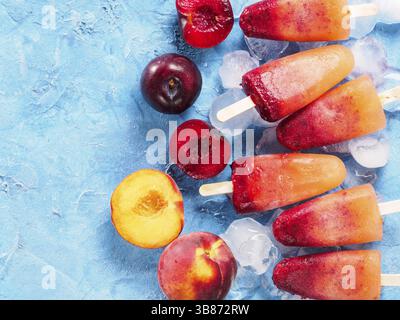 Top view of plum and peach popsicle on blue background. Fruit popsicles ice cream with fresh plums and peach. Copy space Stock Photo