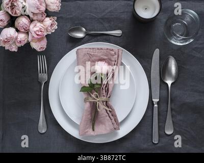 Beautiful table setting with candle on gray linen tablecloth. Festive table setting for wedding dinner with pink spray rose and pink napkin on plate. Stock Photo