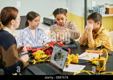 Group of children and instructor engaged in learning robotics in educational setting, focusing on wiring and connecting parts. Classroom background wi Stock Photo