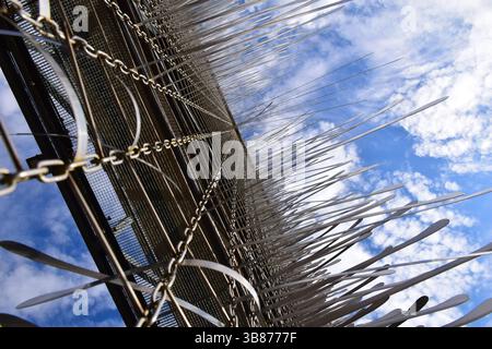 Abstract upward view of a modern metal art installation featuring chains, rods, and mesh. Geometric fence structure and sharp metallic elements. Stock Photo