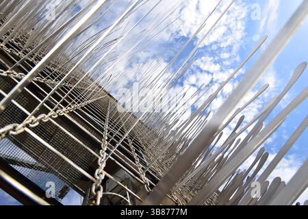 Abstract upward view of a modern metal art installation featuring chains, rods, and mesh. Geometric fence structure and sharp metallic elements. Stock Photo