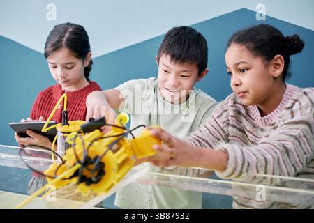 Three children focusing on building and programming robots with colorful parts in engaging classroom environment with concentration and teamwork Stock Photo