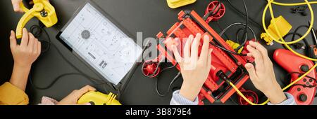 Website header shot of children building robotic gadget using various engineering tools and components on black table with tablet and wires. Hands of Stock Photo
