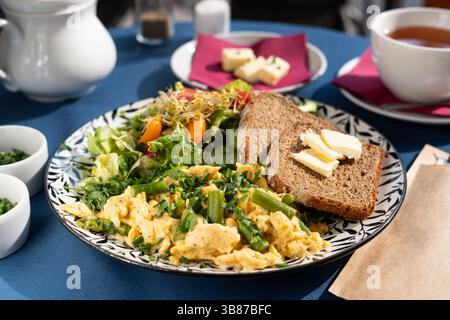Scrambled eggs with vegetables, asparagus, toast, chives, seed sprouts and greens served on a beautifully decorated plate, a breakfast set Stock Photo