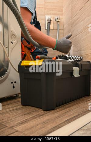 Plumber working on installing a washing machine drain hose, using a toolbox with various tools. Stock Photo