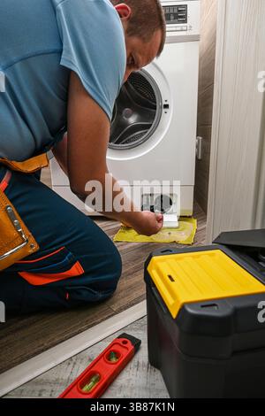 Plumber fixing washing machine filter in bathroom, home appliance maintenance service. Stock Photo