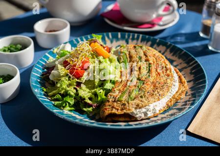 Omelet with cottage cheese and fresh vegetables served on a beautiful blue and white plate. A breakfast set illuminated by the morning sun. Stock Photo
