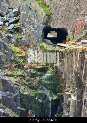 Moss covered rocks and trickling water in the centre of Dinorwic Quarry with the rock tunnel in view, near Llanberis, Snowdonia, Wales, UK. Stock Photo