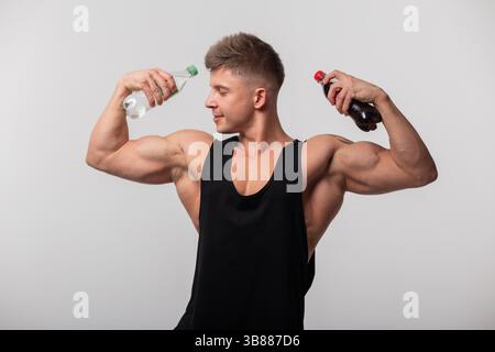 Strong Handsome Muscular Man In Black Tank Top Showing Biceps And Holding Two Sweet Soda Drinks In Studio. Health And Cola Stock Photo