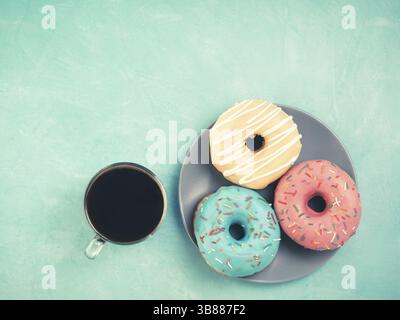 Top view of assorted donuts and coffee on blue concrete background with copy space. Colorful donuts on plate and coffee background. Various glazed dou Stock Photo