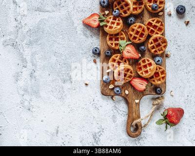 Small round delicious soft belgian waffles on cutting board. Fresh belgian waffles with berries and caramel sauce top view. Copy space for text or moc Stock Photo