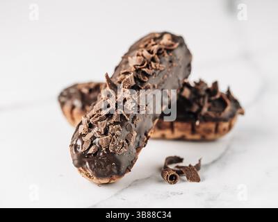 Homemade eclairs with chocolate on white marble background. Close up view of delicious healthy profitroles with chocolate glaze Stock Photo