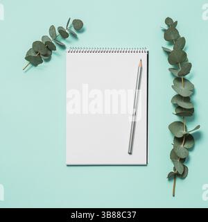 Blank notebook, pencil and eucalyptus on blue background. Empty notebook paper and eucalyptus branch on pastel blue background with copy space for tex Stock Photo